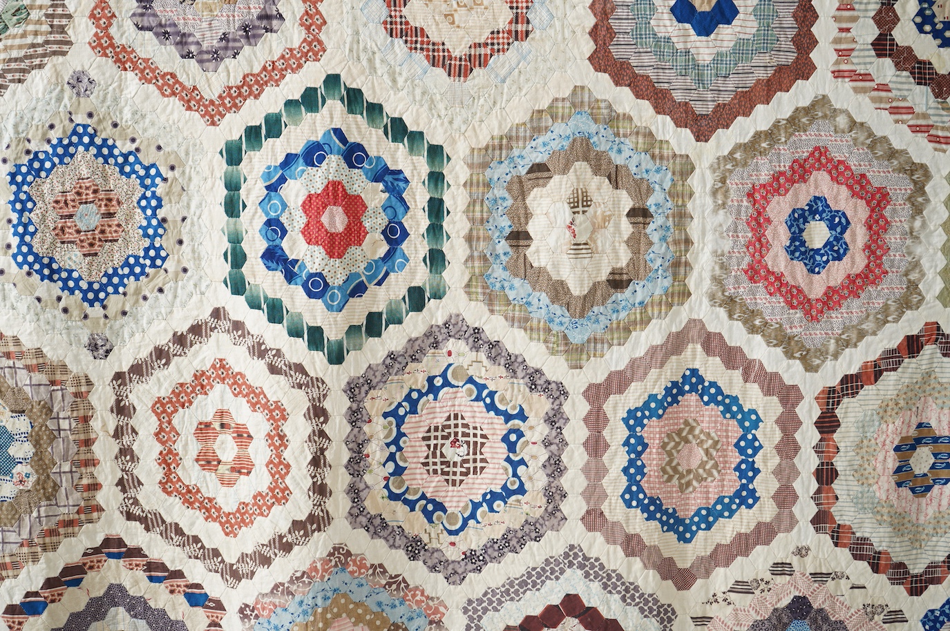 A large 19th century ‘Grandmother’s Flower Garden’ cotton patchwork bedspread, using dress fabric scraps from the day to create hexagonal concentric patterns which form a flower like shape/pattern, 282 x 254cm. Condition